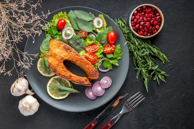 Vista dall'alto gustoso pesce cotto con verdure fresche e condimenti sul tavolo scuro