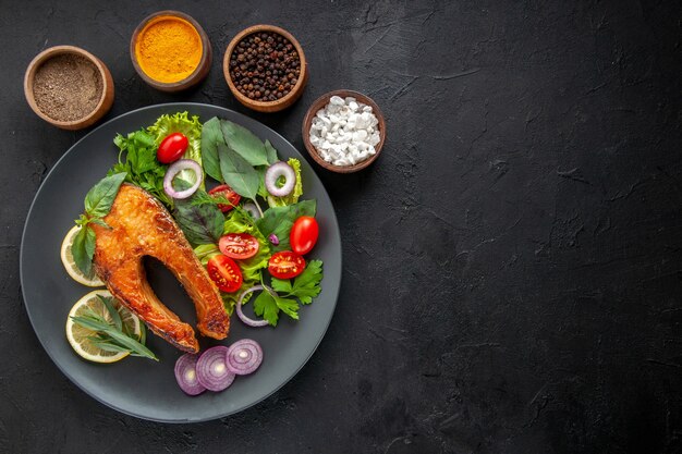 Vista dall'alto gustoso pesce cotto con verdure fresche e condimenti sul tavolo scuro