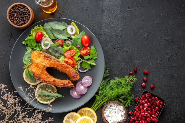 Vista dall'alto gustoso pesce cotto con verdure fresche e condimenti sul tavolo scuro