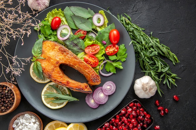 Vista dall'alto gustoso pesce cotto con verdure fresche e condimenti sul tavolo scuro