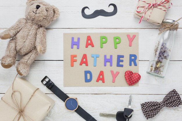Vista dall'alto Happy Father's day concept.Pen con la parola "FELICE GIORNATA DI PADRE" su fondo in legno.Accessori con baffi, cravatta d'archi vintage, bambola orso, fiore essiccato, chiave e presente per il regalo.
