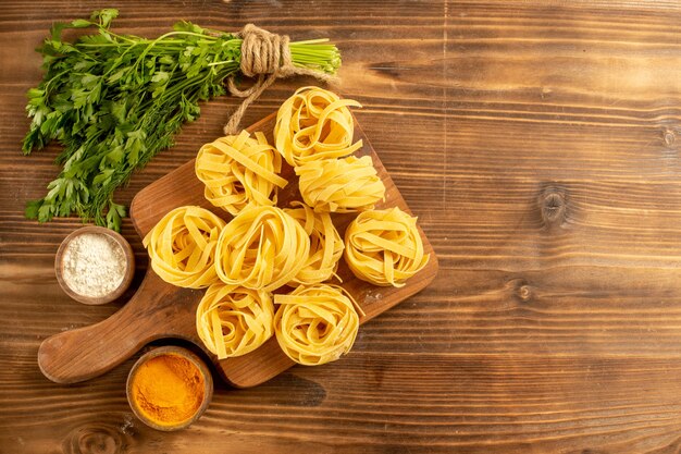 Vista dall'alto impasto di pasta cruda con condimenti e verdure sulla pasta alimentare farina di sfondo marrone