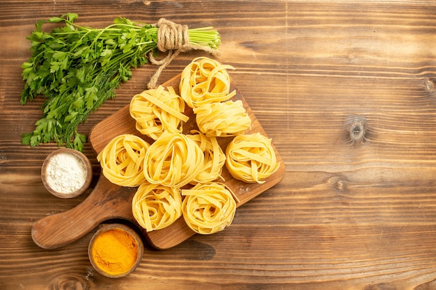 Vista dall'alto impasto di pasta cruda con condimenti e verdure sulla pasta alimentare farina di sfondo marrone