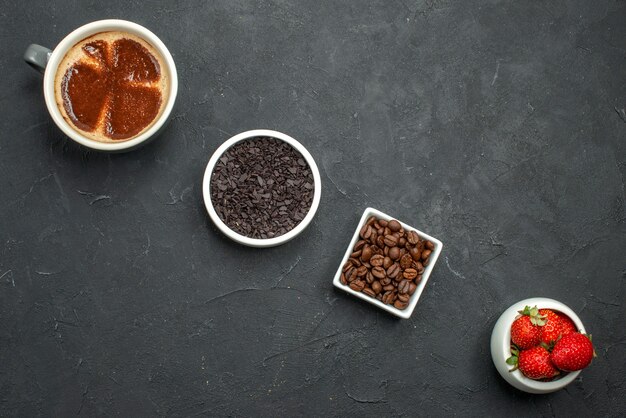 Vista dall'alto in diagonale una tazza di ciotole di caffè con semi di caffè al cioccolato e fragole su sfondo scuro