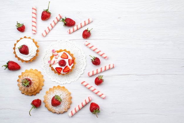 Vista dall'alto in lontananza piccola torta con crema e fragole a fette caramelle sulla scrivania bianca, torta di frutta bacca dolce zucchero cuocere