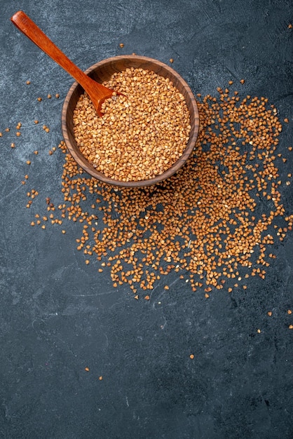 Vista dall'alto ingredienti freschi di grano saraceno crudo all'interno del piatto marrone su spazio grigio