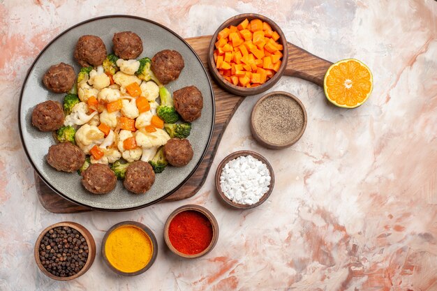 Vista dall'alto insalata di broccoli e cavolfiore e polpetta su piatto taglio carota in ciotola fetta di limone sul tagliere spezie diverse in piccole ciotole su sfondo nudo spazio libero