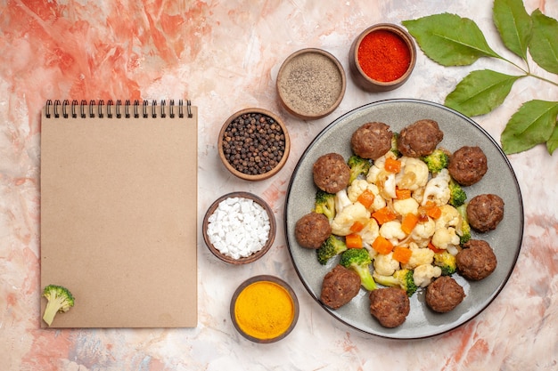 Vista dall'alto insalata di broccoli e cavolfiore e polpetta sul piatto spezie diverse in piccole ciotole un quaderno su sfondo nudo isolato