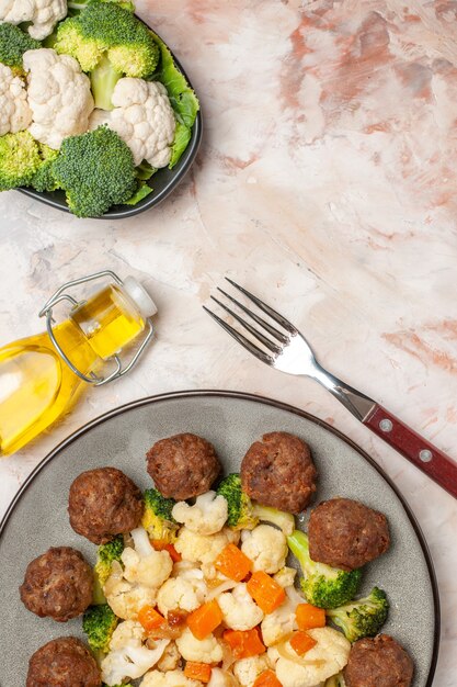 Vista dall'alto insalata di broccoli e cavolfiore e polpetta sul piatto tovagliolo a scacchi verde e bianco una forchetta bottiglia di olio verdure crude sul piatto su sfondo nudo isolato