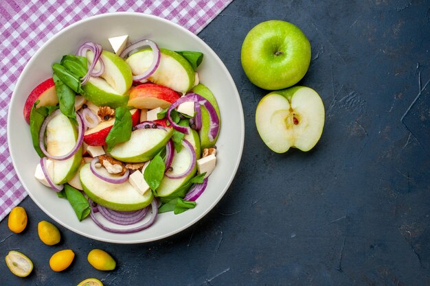 Vista dall'alto insalata di mele fresca su piatto rotondo mele cumcuat tovaglia a quadretti viola e bianca sul tavolo scuro