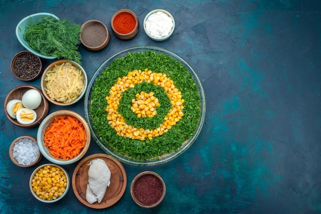 Vista dall'alto insalata di verdure con mais insieme a condimenti e uova su sfondo blu scuro.