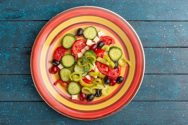 Vista dall'alto insalata di verdure fresche con cetrioli affettati pomodori oliva e formaggio bianco all'interno del piatto con pomodori sulla superficie blu scuro cibo vegetale insalata pasto spuntino