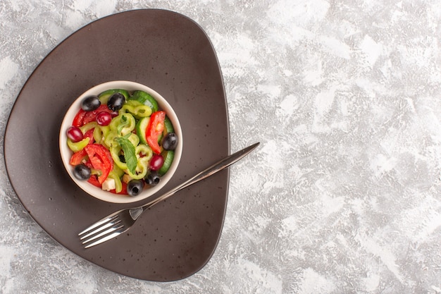 Vista dall'alto insalata di verdure fresche con cetrioli affettati pomodori oliva e formaggio bianco all'interno della piastra marrone sul pasto di insalata di cibo vegetale grigio scrivania rustica