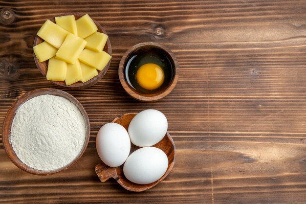 Vista dall'alto intere uova crude con farina e formaggio su tavola marrone pasta all'uovo pasta sfoglia farina di farina