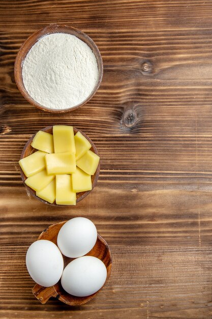 Vista dall'alto intere uova crude con farina e formaggio sul tavolo marrone pasta all'uovo farina di prodotti in polvere