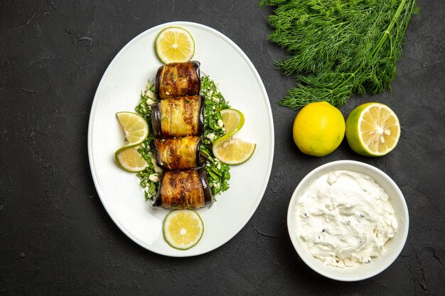 Vista dall'alto involtini salati di melanzane piatto cucinato con fette di limone su fondo scuro piatto da cucina con olio per cena