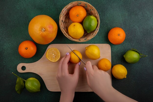 Vista dall'alto la donna taglia i limoni sul tagliere con limes arance e pompelmi su sfondo verde