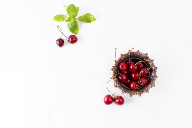 Vista dall'alto le ciliege acide rosse all'interno della zolla marrone sulla foto pastosa del succo di colore della frutta del fondo bianco