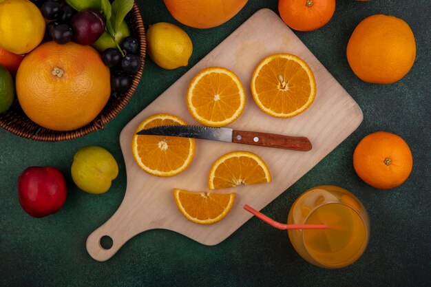 Vista dall'alto le fette di arancia su un tagliere con un coltello pompelmo lime limone prugna e pesca in un cesto su uno sfondo verde