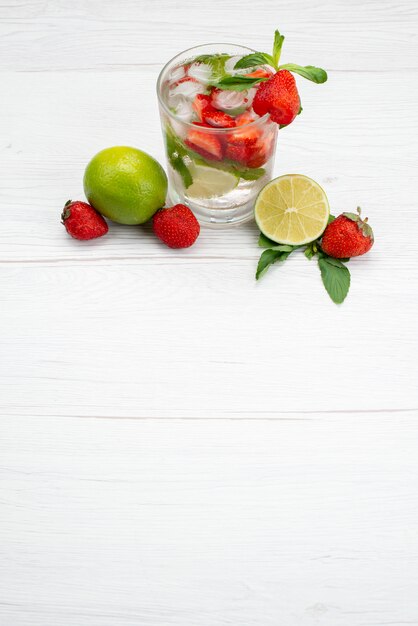 Vista dall'alto lime e fragole fresche e morbide con un bicchiere d'acqua su bianco, frutti di bosco bere agrumi