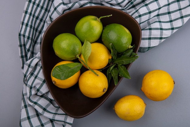 Vista dall'alto limette con limoni in una ciotola su un asciugamano a scacchi su uno sfondo grigio