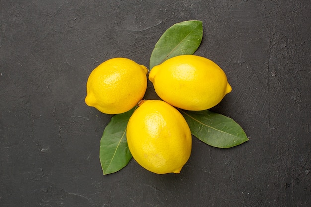 Vista dall'alto limoni freschi aspri con foglie sul tavolo scuro agrumi giallo lime frutta