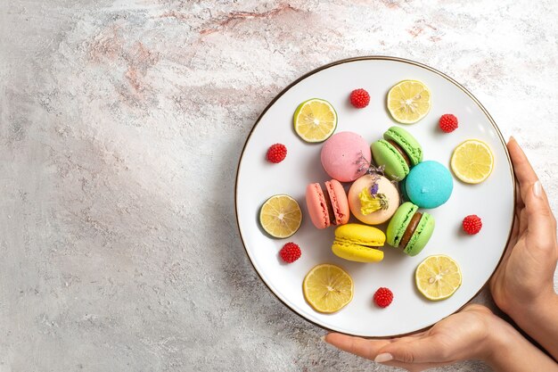 Vista dall'alto macarons francesi piccole torte deliziose con fettine di limone su superficie bianca chiara biscotto torta biscotto zucchero dolce