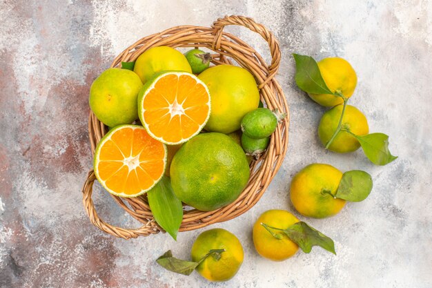 Vista dall'alto mandarini freschi in cesto di vimini circondati da mandarini su sfondo nudo
