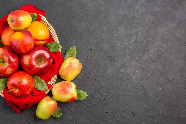 Vista dall'alto mele fresche con pesche all'interno del cesto su tavola scura frutta matura fresca