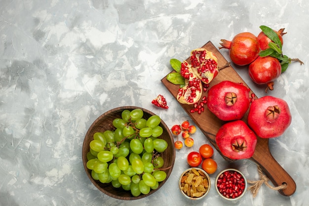 Vista dall'alto melograni rossi freschi frutti aspri e pastosi con uva verde fresca sulla scrivania bianco chiaro