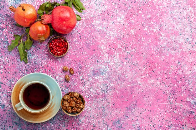 Vista dall'alto melograno fresco con foglie verdi e tazza di tè sulla superficie rosa