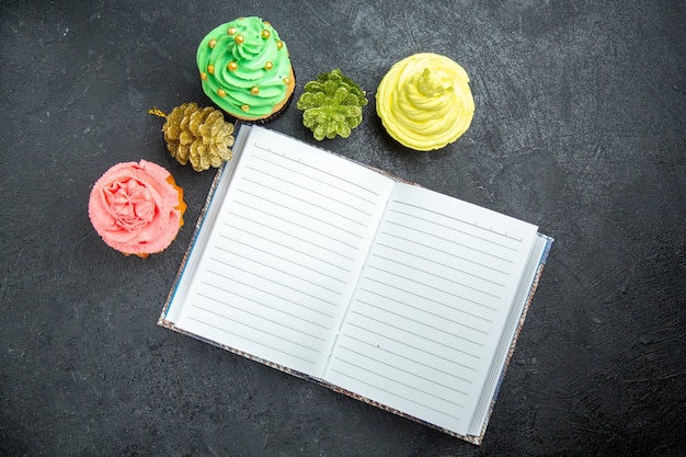 Vista dall'alto mini cupcakes colorati e un quaderno su una superficie scura