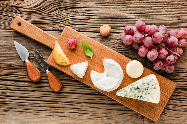 Vista dall'alto mix di formaggi gourmet sul tagliere di legno con uva e utensili