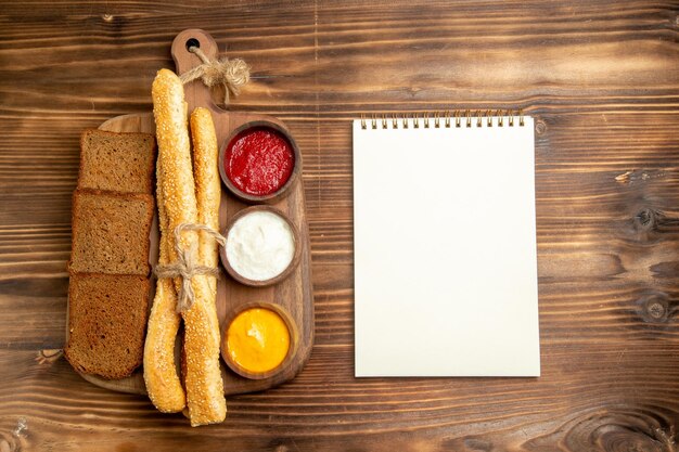 Vista dall'alto pagnotte di pane scuro con blocco note di panini e condimenti su panino di pane da scrivania marrone piccante