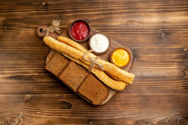 Vista dall'alto pagnotte di pane scuro con focacce e condimenti sul panino di pane da scrivania marrone piccante