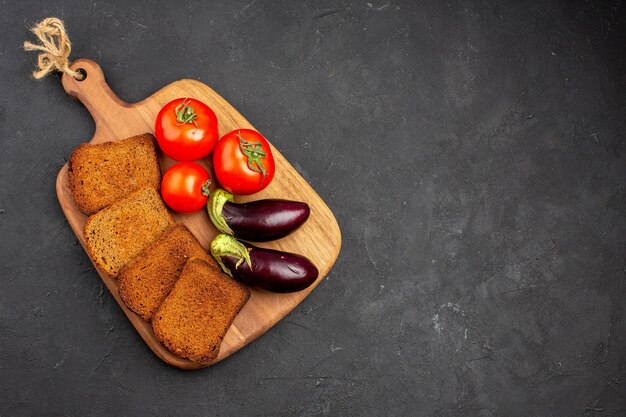 Vista dall'alto pagnotte di pane scuro con pomodori e melanzane sul pasto maturo per la salute dell'insalata di sfondo scuro