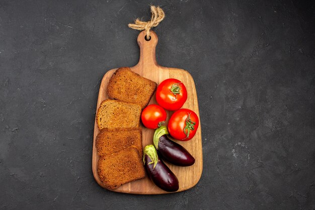 Vista dall'alto pagnotte di pane scuro con pomodori e melanzane sul pasto maturo per la salute dell'insalata di sfondo scuro