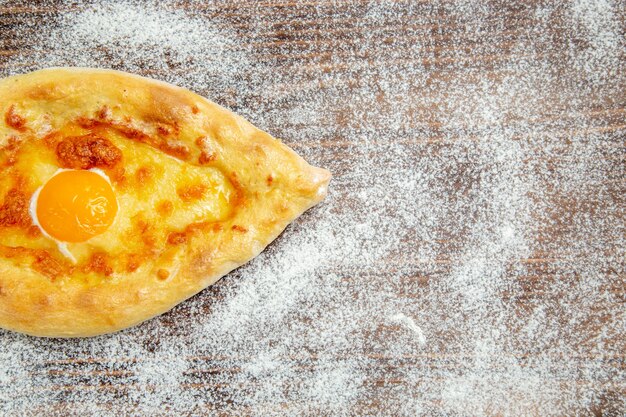 Vista dall'alto pane appena sfornato con uova cotte e farina sulla pasta da scrivania marrone cuocere l'uovo del pasto del panino