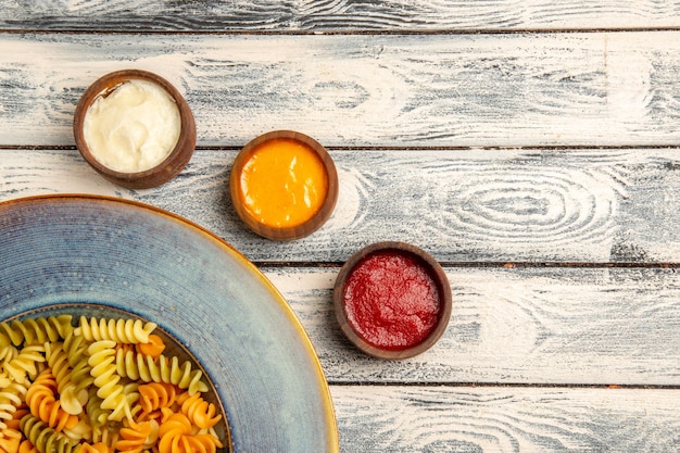 Vista dall'alto pasta a spirale cotta con diversi condimenti sulla scrivania grigia pasta pasta color pepe cibo