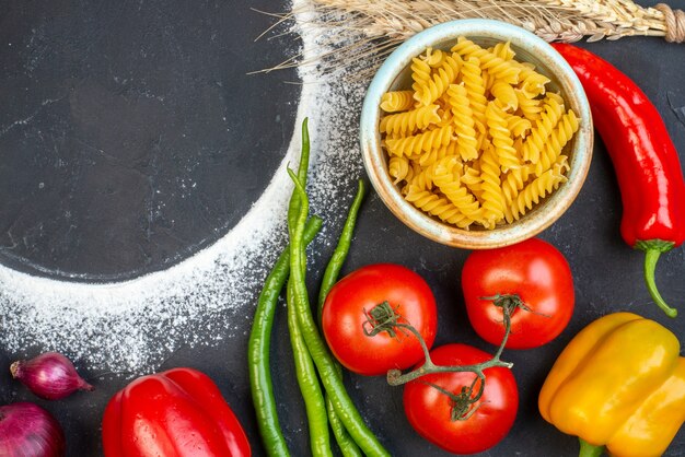 Vista dall'alto pasta a spirale del cerchio di farina cosparsa in una ciotola pomodori verdi e peperoni roventi cipolla rossa sul tavolo spazio libero