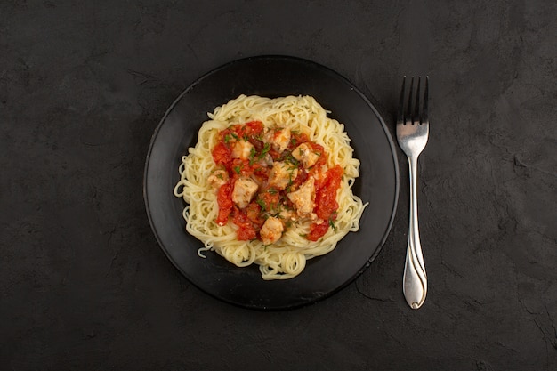 vista dall'alto pasta con ali di pollo e salsa di pomodori all'interno della banda nera sul pavimento scuro