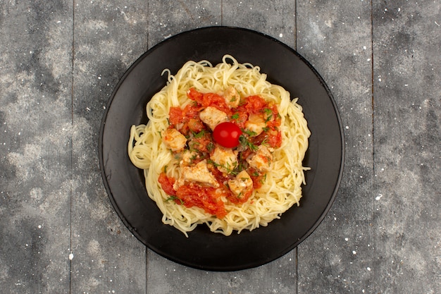 vista dall'alto pasta cotta con salsa di pomodoro e ali di pollo a fette all'interno della banda nera sul pavimento di legno rustico grigio