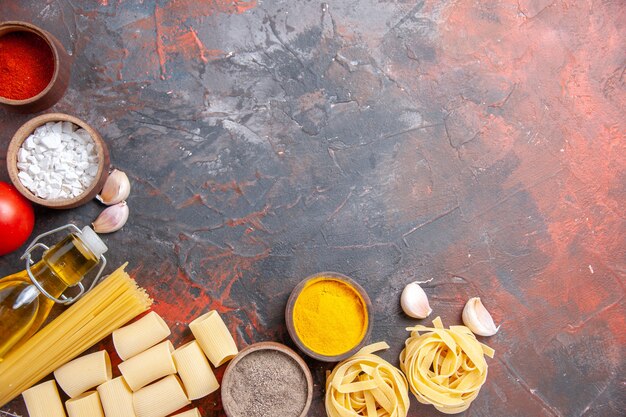 Vista dall'alto pasta cruda con diversi ingredienti sull'impasto per pasta di colore superficie scura