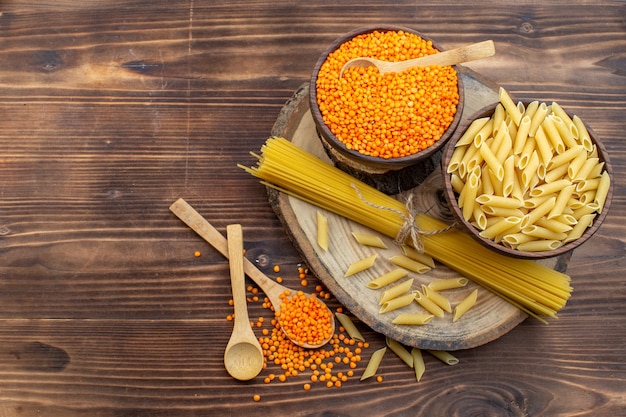 Vista dall'alto pasta cruda con lenticchie arancioni su superficie marrone