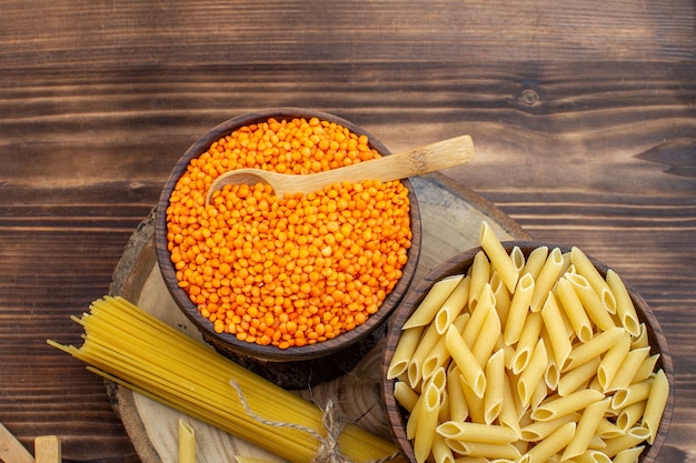 Vista dall'alto pasta cruda con lenticchie arancioni su superficie marrone