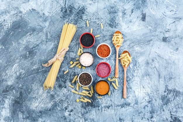 Vista dall'alto pasta cruda con spezie, cucchiai di legno su sfondo grigio intonaco. orizzontale