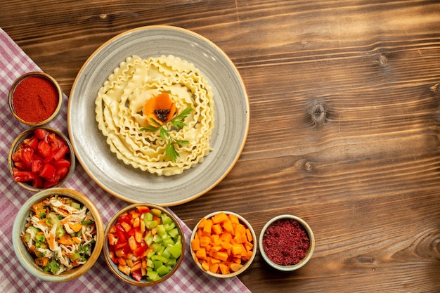 Vista dall'alto pasta di pasta cruda con verdure e condimenti sul pasto di pasta di cibo crudo di pasta da tavola marrone