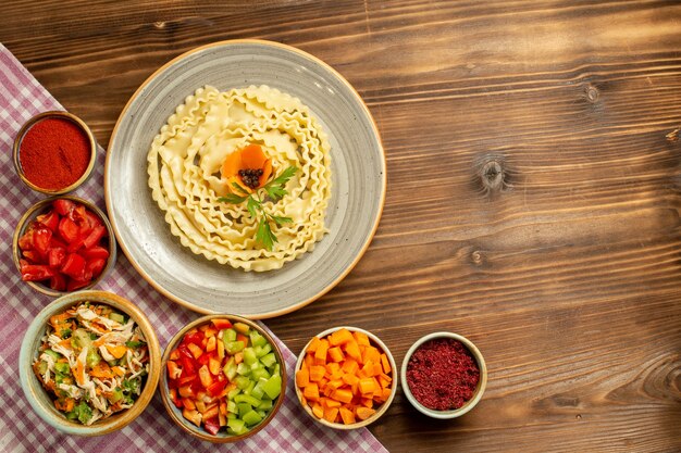 Vista dall'alto pasta di pasta cruda con verdure e condimenti sul pasto di pasta di cibo crudo di pasta da tavola marrone