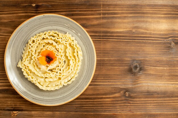 Vista dall'alto pasta di pasta cruda formata all'interno del piatto sulla pasta di farina di cibo crudo di pasta da tavola marrone