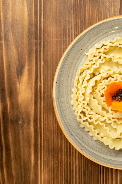 Vista dall'alto pasta di pasta cruda formata all'interno del piatto sulla pasta di farina di cibo crudo di pasta da tavola marrone